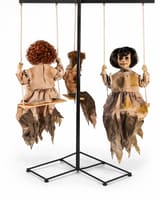 Three creepy child figures seated on swings in a freestanding Halloween prop frame