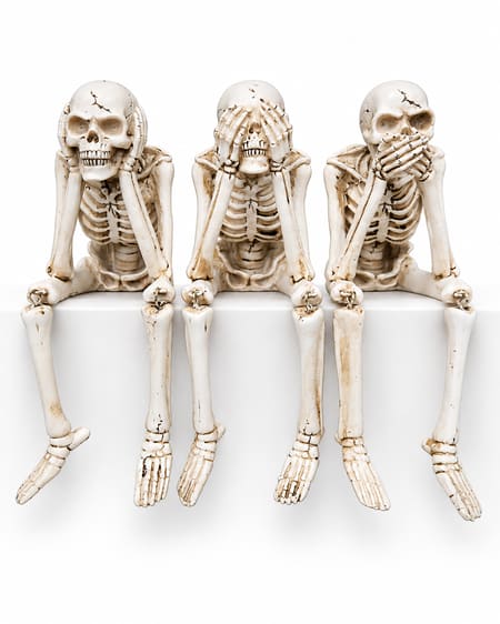 Set of three aged bone-coloured skeleton shelf sitters covering ears, eyes and mouth, with dangling legs