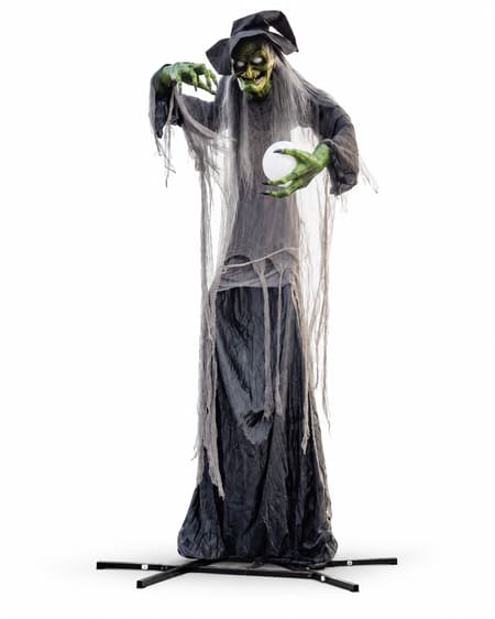 Giant green-faced witch animatronic with black hat, grey hair, tattered black dress and crystal ball on a metal floor stand