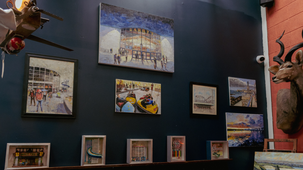 Image of part of our artist showcase. Several of Paul Gallagher's artworks hanging on a wall. They depict scenes from Barry's and the North Coast.