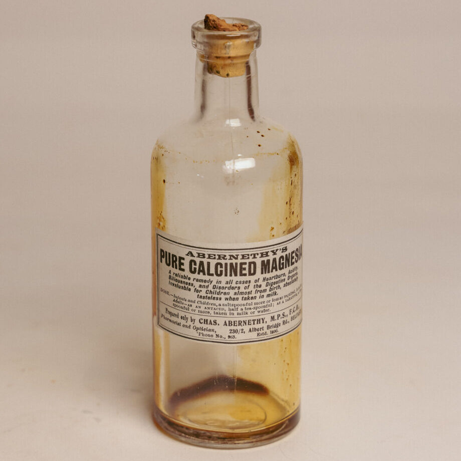 A clear bottle with a cork and some brown residue inside. The label reads "pure calcined magnesia."