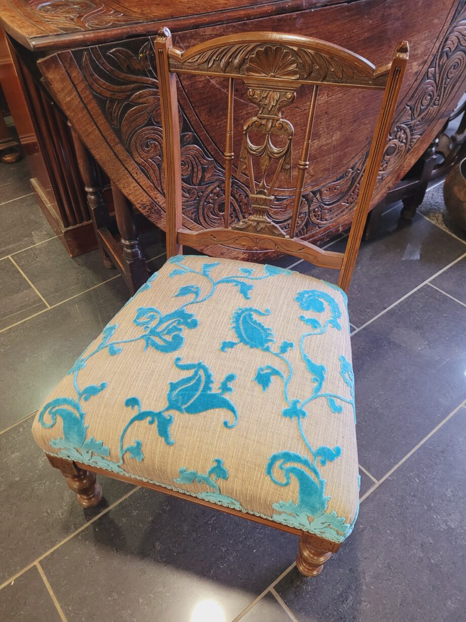 A wooden Edwardian nursing chair with a reupholstered seat in a cream and ble fabric