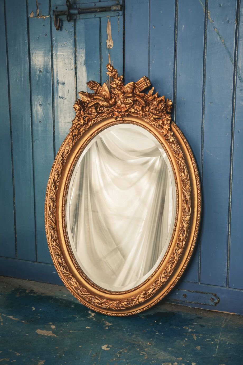 An oval mirror with a gold frame and a bird on top.