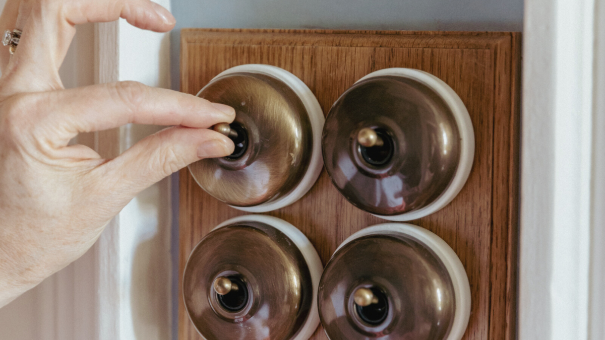 A woman's hand turning on a brass light switch. 