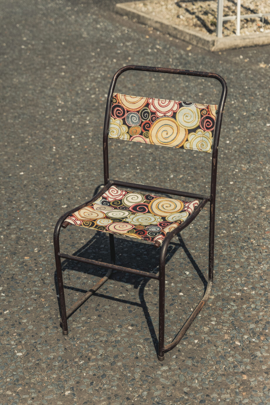 A metal chair with a reupholstered back and seat in a colourful spiral fabric